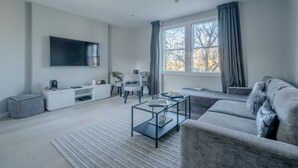 Een moderne woonkamer met een flatscreen televisie, een bank, een salontafel en een raam met gordijnen.