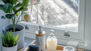 Uitzicht vanuit een raam op een besneeuwde straat met geparkeerde auto's, een potplant, een marmeren doos, een zeepdispenser en een dienblad met een kopje en onderzetters.
