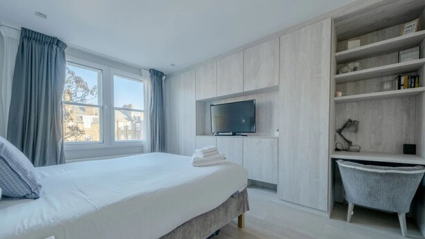 Een moderne hotelkamer met een groot bed, een aan de muur bevestigde televisie, een bureau met stoel en een inbouwkast.