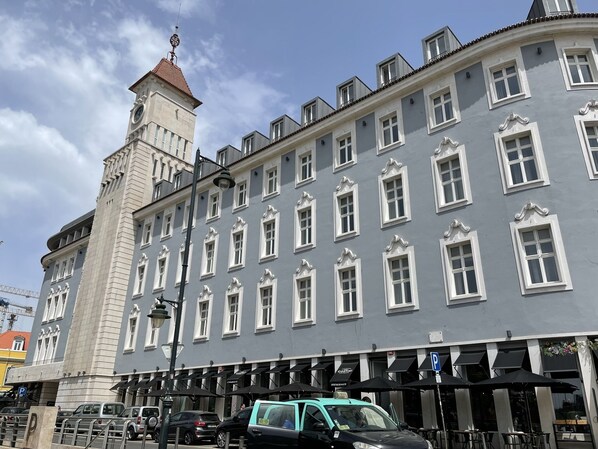 A historic building with a clock tower, multiple windows, and outdoor seating with umbrellas.