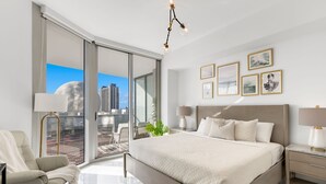 A modern bedroom with a large bed, a sofa, a desk, and a balcony with a city view.