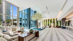 A modern hotel lobby with large windows, a central seating area, a reception desk, and a green wall with vertical gardens.