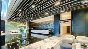 A modern lobby with a reception desk, seating area, and a decorative plant arrangement.