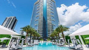 A high-rise hotel with a modern design, featuring a central pool surrounded by lounge chairs and palm trees.