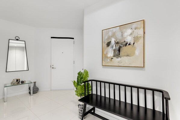 A modern interior with a black bench, a glass console table, a potted plant, and a large abstract painting on the wall.