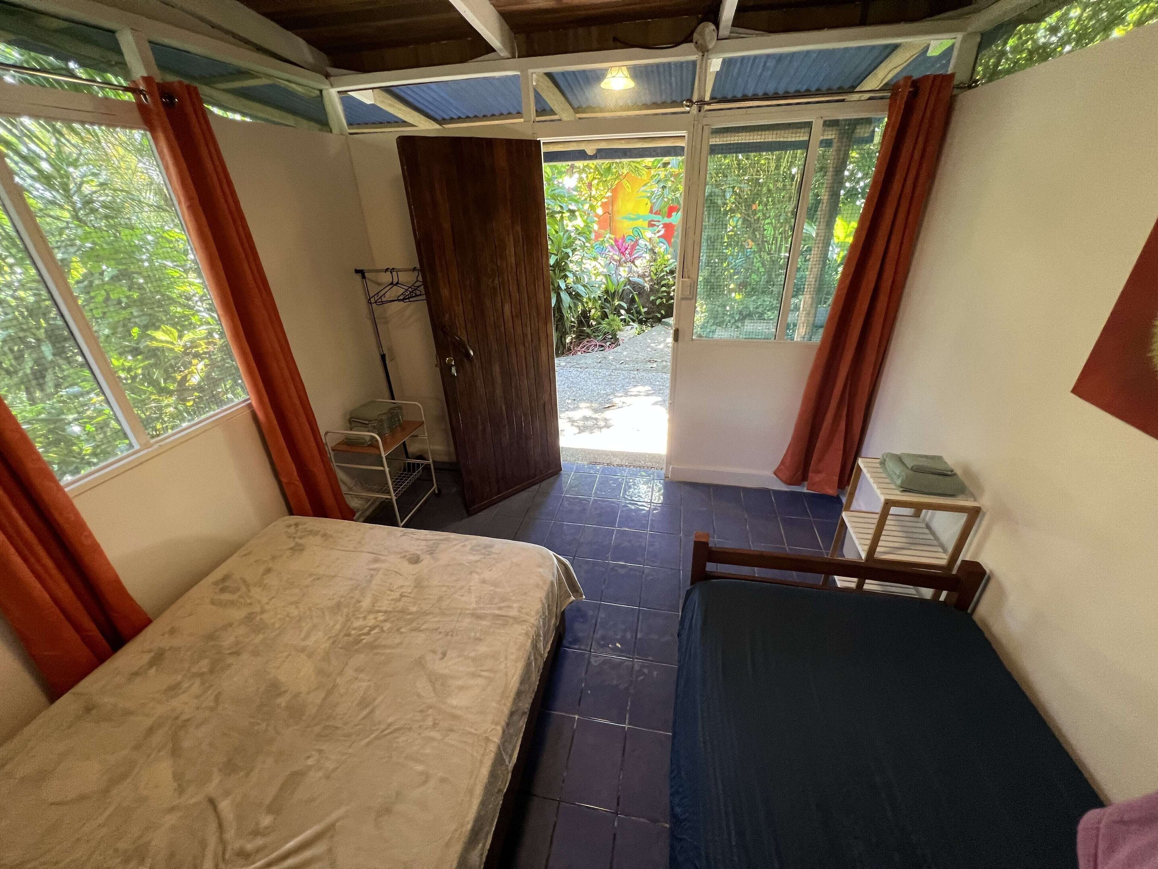 A room with two beds, a wooden door, and a window with curtains.