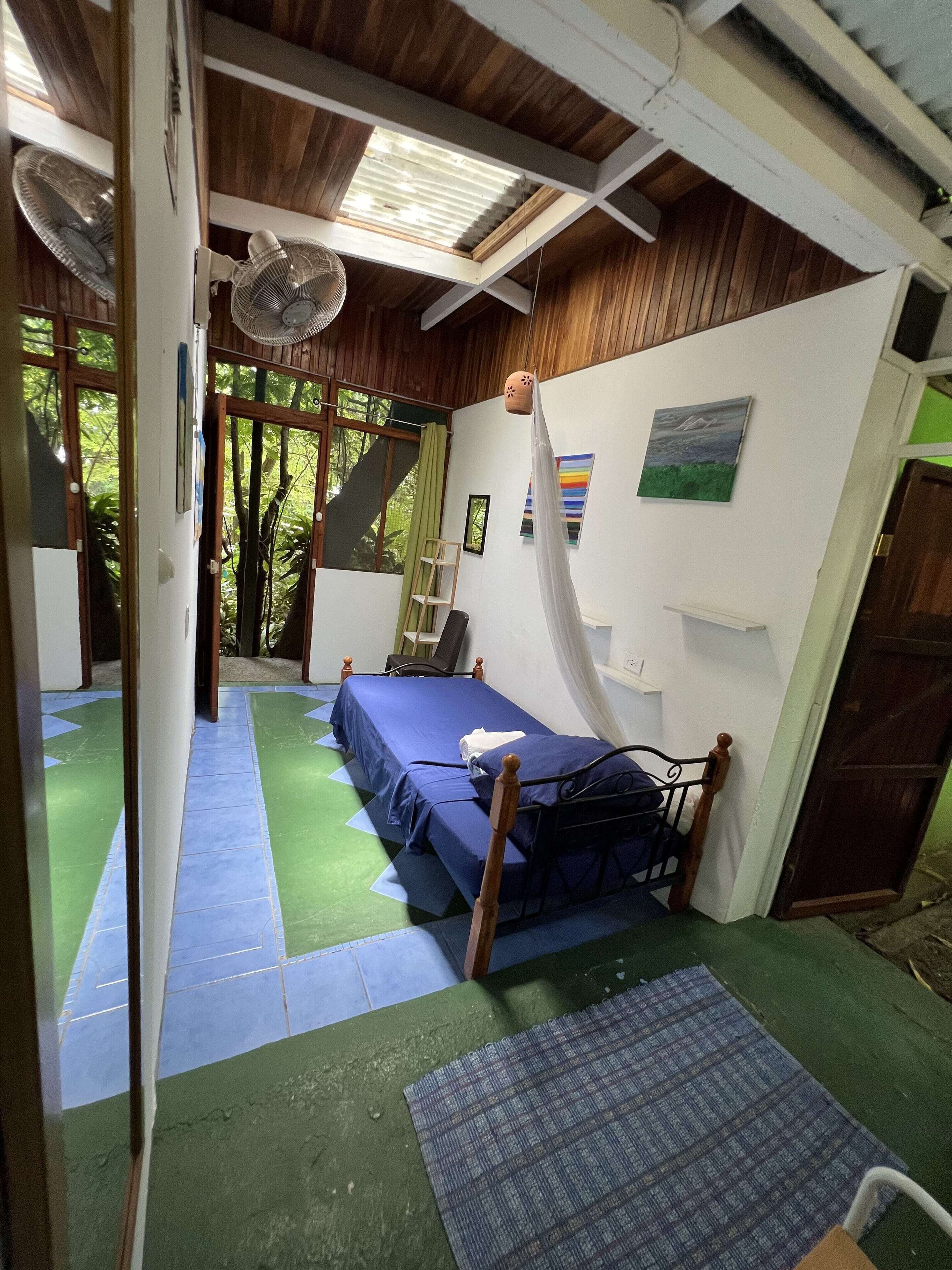 A room with a bed, a fan, a ladder, and a view of the outdoors.