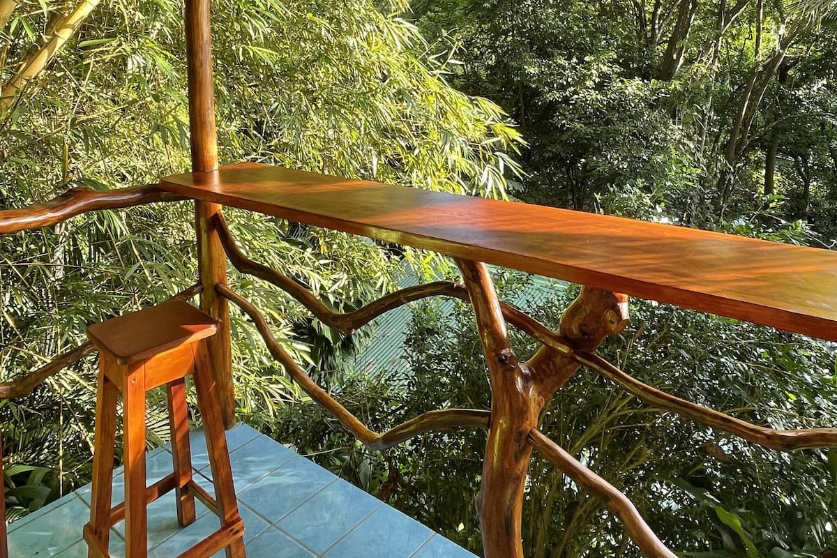A wooden deck with a bench and a table, surrounded by lush greenery.