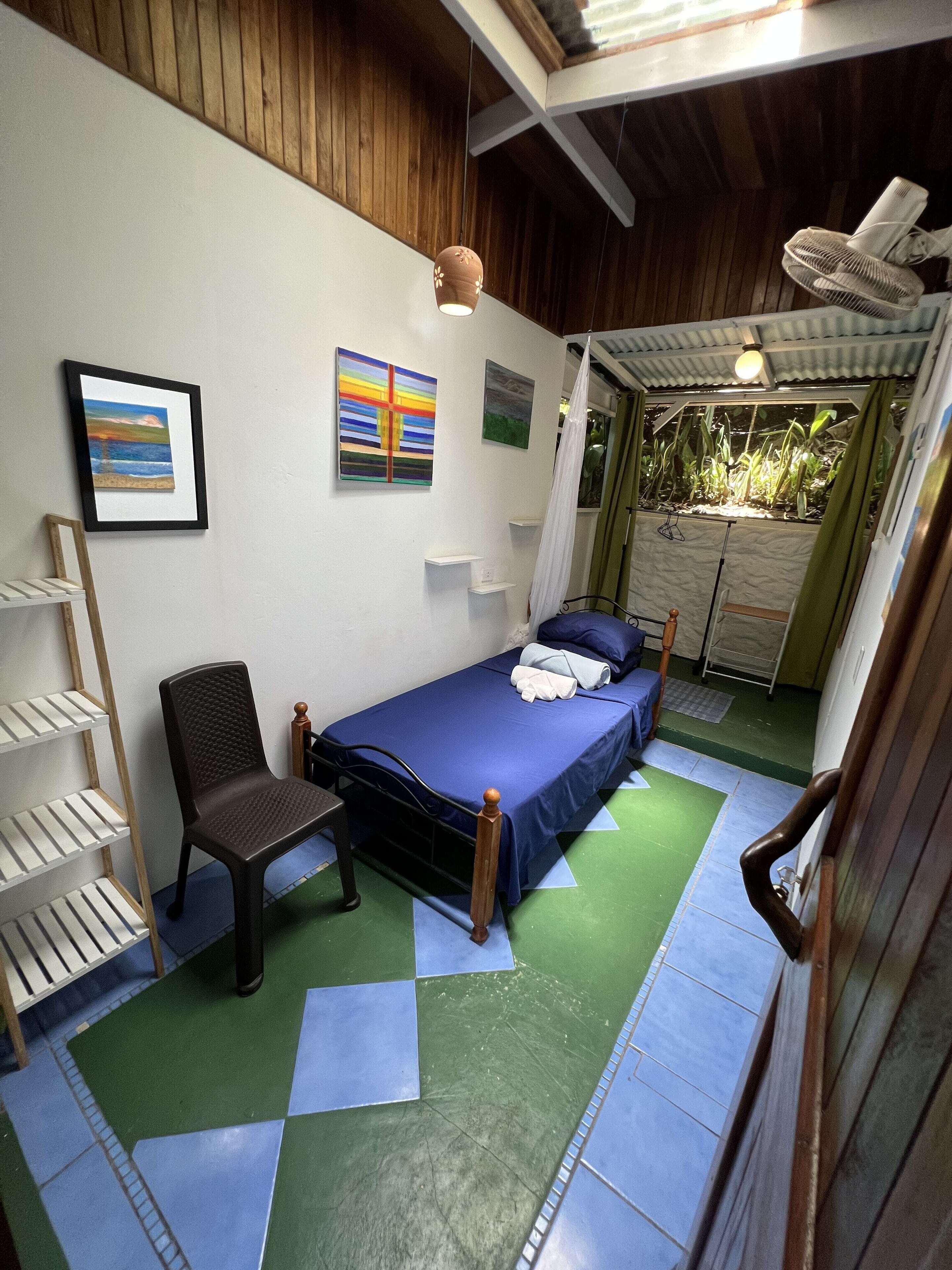 A room with a bed, a chair, a shelf, and artwork on the wall.