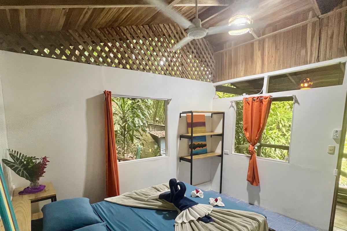 A bedroom with a bed, a ceiling fan, a shelf with towels, and a window with curtains.