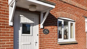 A brick house with a white door and window, a mailbox, and a house number sign. - Mead Cottage (Bridport)
