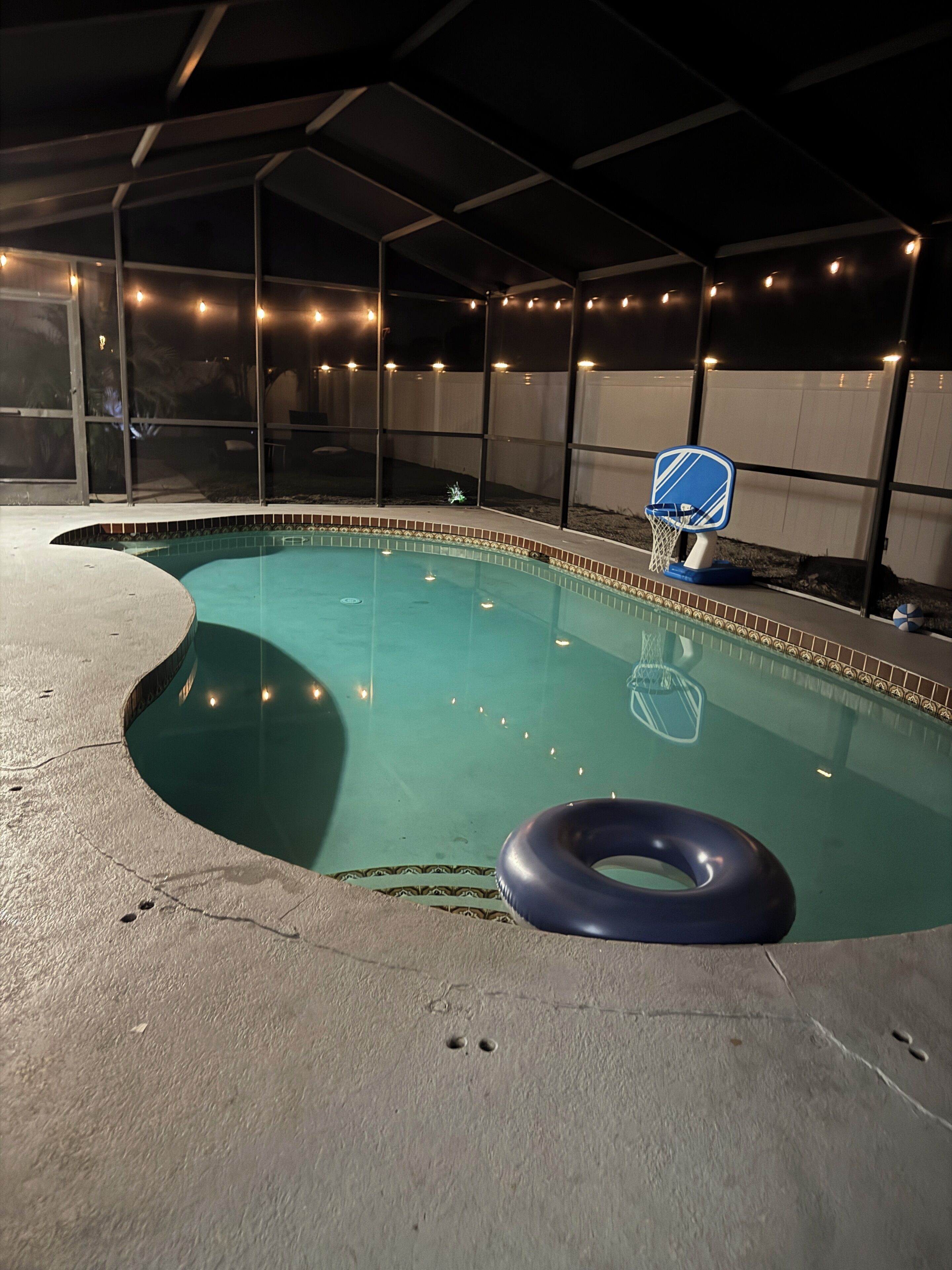 En swimmingpool med en blå oppustelig ring, en lille basketballkurv og lyskæder.