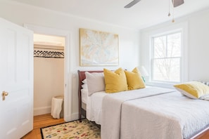 Un dormitorio con cama, ventana, puerta y un cuadro en la pared.
