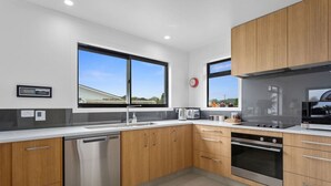 A modern kitchen with wooden cabinets, stainless steel appliances, and large windows. - Kate and Harry's - Waiotahe (Opotiki)