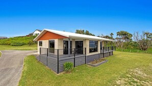 A modern single-story house with a covered porch, a fenced yard, and a well-maintained lawn. - Kate and Harry's - Waiotahe (Opotiki)
