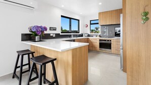 A modern kitchen with a central island, wooden cabinets, stainless steel appliances, and a view of the outdoors. - Kate and Harry's - Waiotahe (Opotiki)