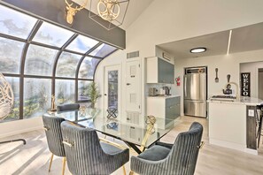 A modern kitchen with a glass dining table, stainless steel appliances, and a view through a large window.