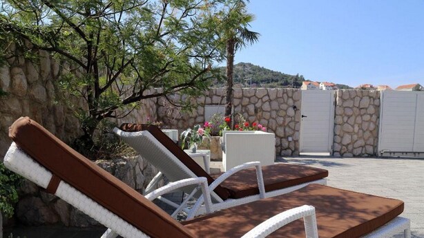 Two lounge chairs with brown cushions, a stone wall, and a view of a mountain in the background.