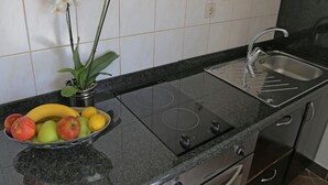 A kitchen with a black countertop, a stainless steel sink, a bowl of fruit, and white orchids on the wall.