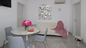 A modern living room with a round marble table, two chairs, a sofa with a pink blanket, a decorative mirror, and a clock on the wall.