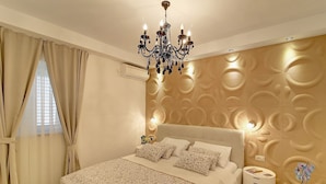 A bedroom with a large bed, a chandelier, a wall with a textured pattern, and a bedside table with a lamp. - Villa Vanda - Deluxe Two Bedroom Apartment with Swimming Pool (Dubrovnik)