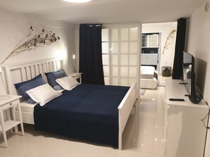 Une chambre à coucher comprenant un lit, des tables de chevet, un bureau, une chaise, un téléviseur, et une salle de bain visible à travers une porte ouverte.