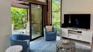 Una sala de estar moderna con un televisor grande, asientos cómodos y vistas al verde exterior.