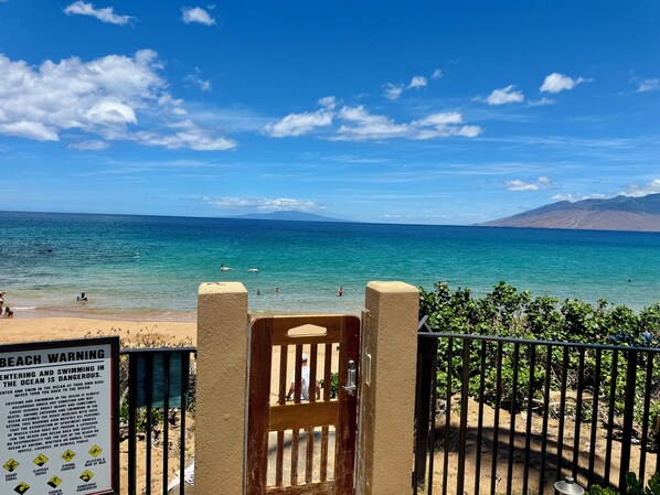 A beach with a warning sign, a gate, and a view of the ocean and mountains. - Luxury 1 Bed 2 Bath Direct Ocean Front Property - 5 Star -  Sleeps 4 - Sleeps 4 (Kihei)