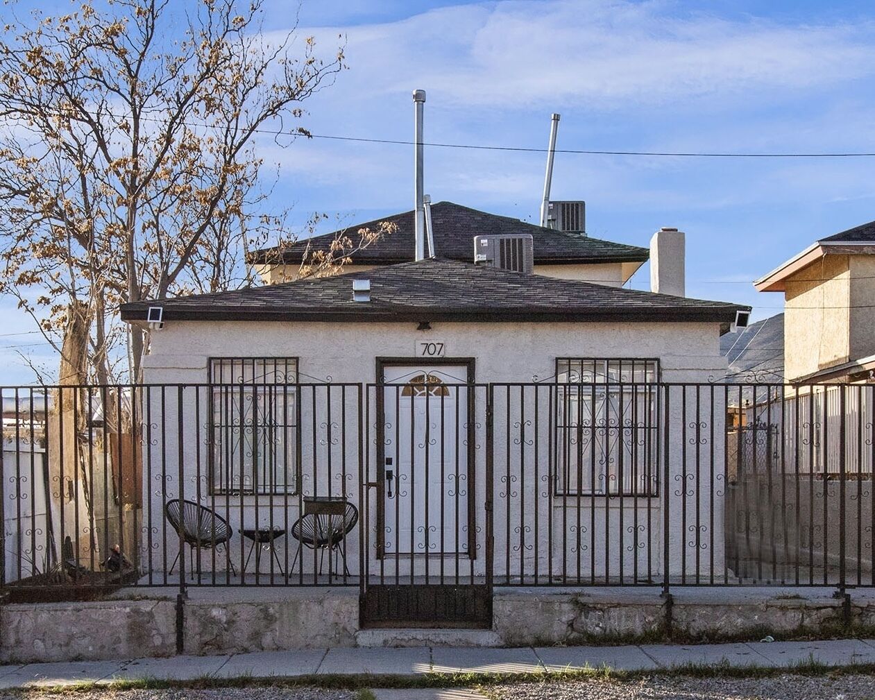 Ein kleines Haus mit der Nummer 707 an der Tür, einem eingezäunten Garten und einem Baum.