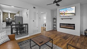 Una sala de estar moderna con chimenea, un televisor montado encima y un comedor con cocina al fondo.