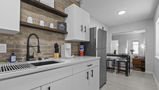 Una cocina moderna con armarios blancos, un refrigerador de acero inoxidable y una pared decorada con ladrillos.