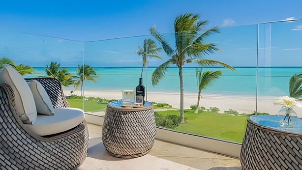 A balcony with wicker furniture, a bottle, and a view of the beach and ocean. - Punta Palmera Beach Front with private cold jacuzzI (Punta Cana)