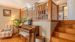 A wooden staircase, a piano, a striped armchair, and a potted plant in a living room.