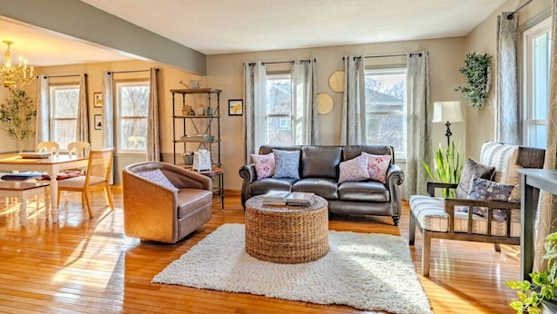A living room with a sofa, armchair, and a coffee table, wooden flooring, and a large window with curtains.