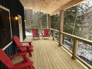 Une terrasse en bois avec des fauteuils Adirondack rouges, une balustrade en bois et une vue sur une forêt enneigée.
