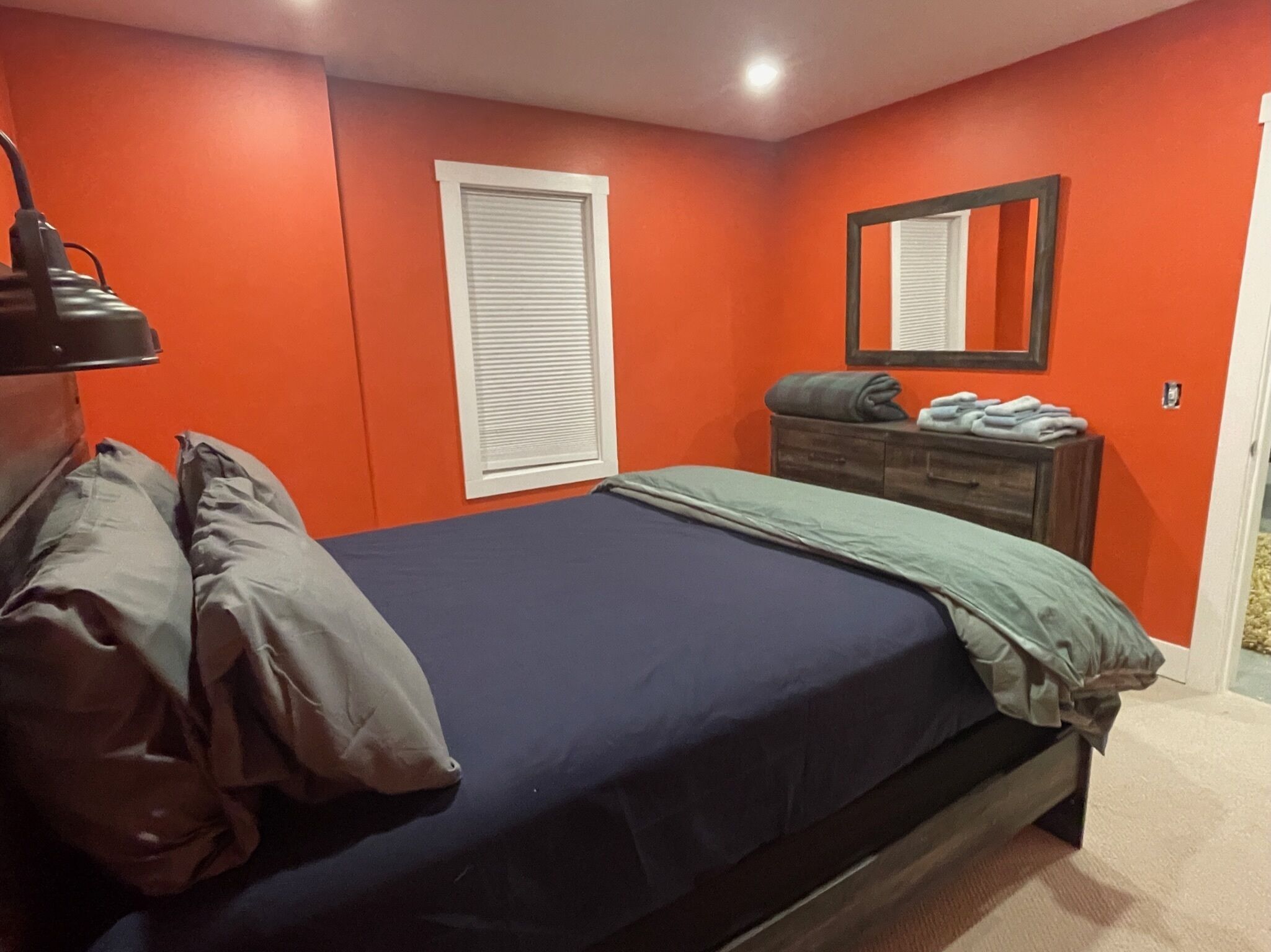 Un dormitorio con cama, cómoda, espejo y ventana con persianas.