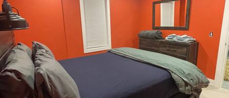 Un dormitorio con cama, cómoda, espejo y ventana con persianas.