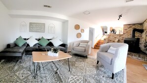 Un saló amb un sofà, butaques, una taula de centre i una catifa amb un disseny. Hi ha una escala que mena a una zona en alt amb una paret de maó i una llar de foc.