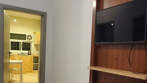 A room with a wooden coffee table, a purple throw, a wall-mounted TV, and a clock.