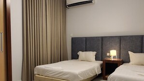 A hotel room with two beds, a ceiling light, an air conditioning unit, and a wooden door.