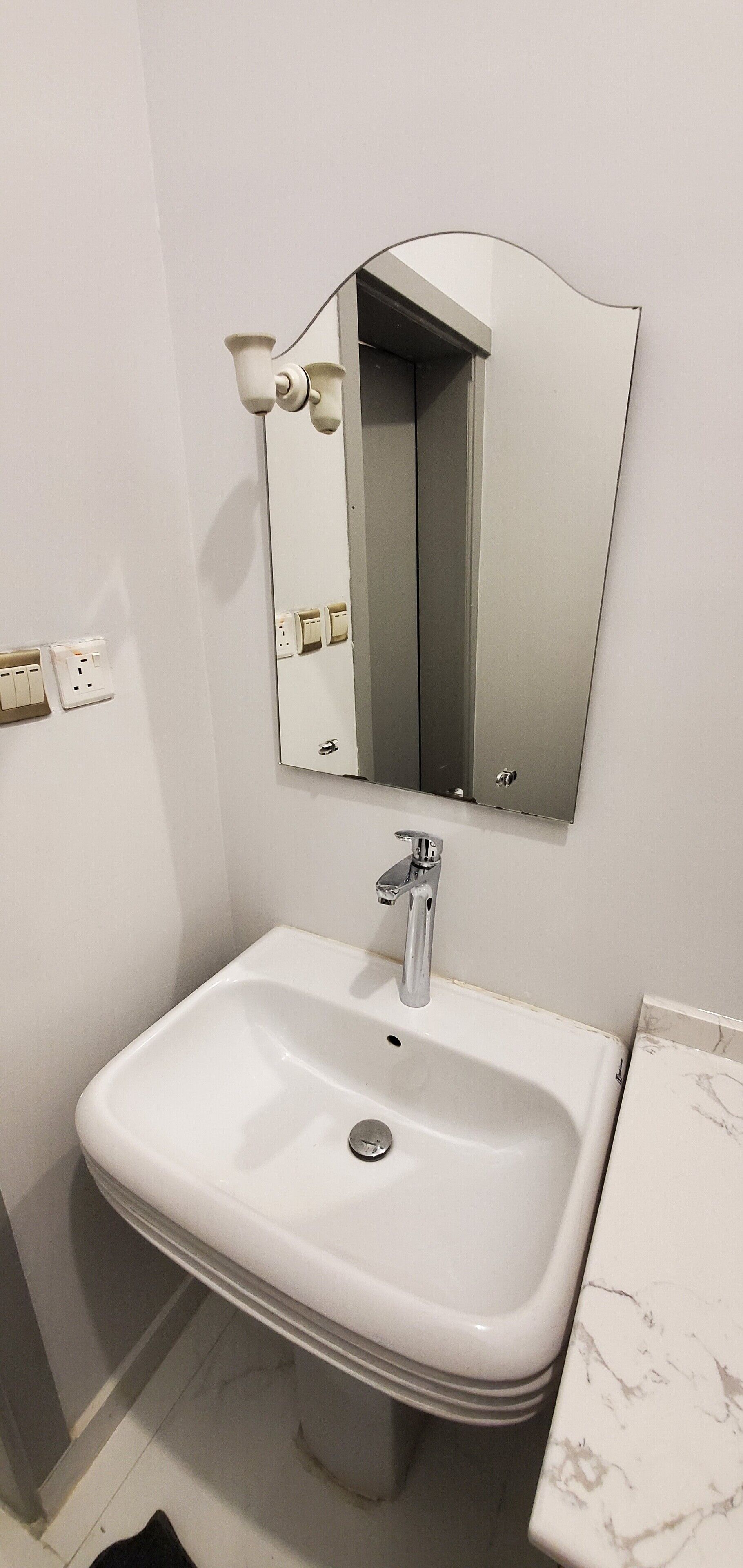 Een badkamer met een witte wastafel, een spiegel en een marmeren aanrecht.