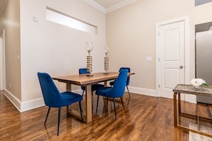 A dining area with a wooden table and blue chairs, a small side table with a vase, and a white door in the background.