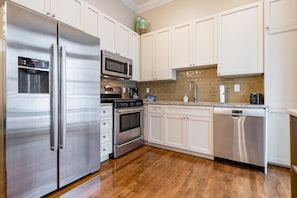 A modern kitchen with stainless steel appliances, white cabinetry, and a tiled backsplash.