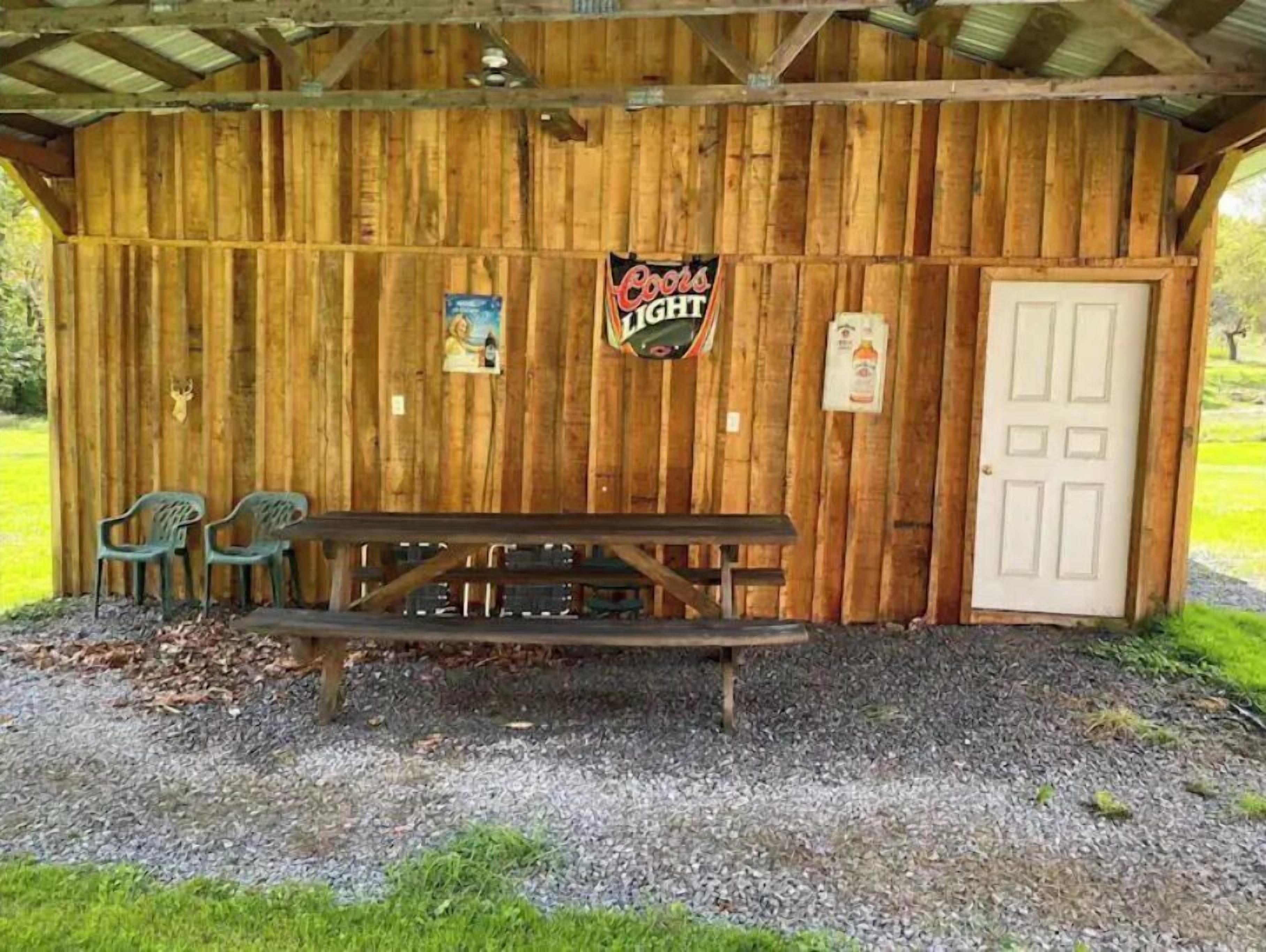A wooden cabin with a picnic table and two chairs, a Coors Light sign, and a door.