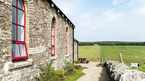A stone building with red-framed windows and a gravel path leading to a picnic table. - Chapel on the Hill (FOREST IN TEESDALE)