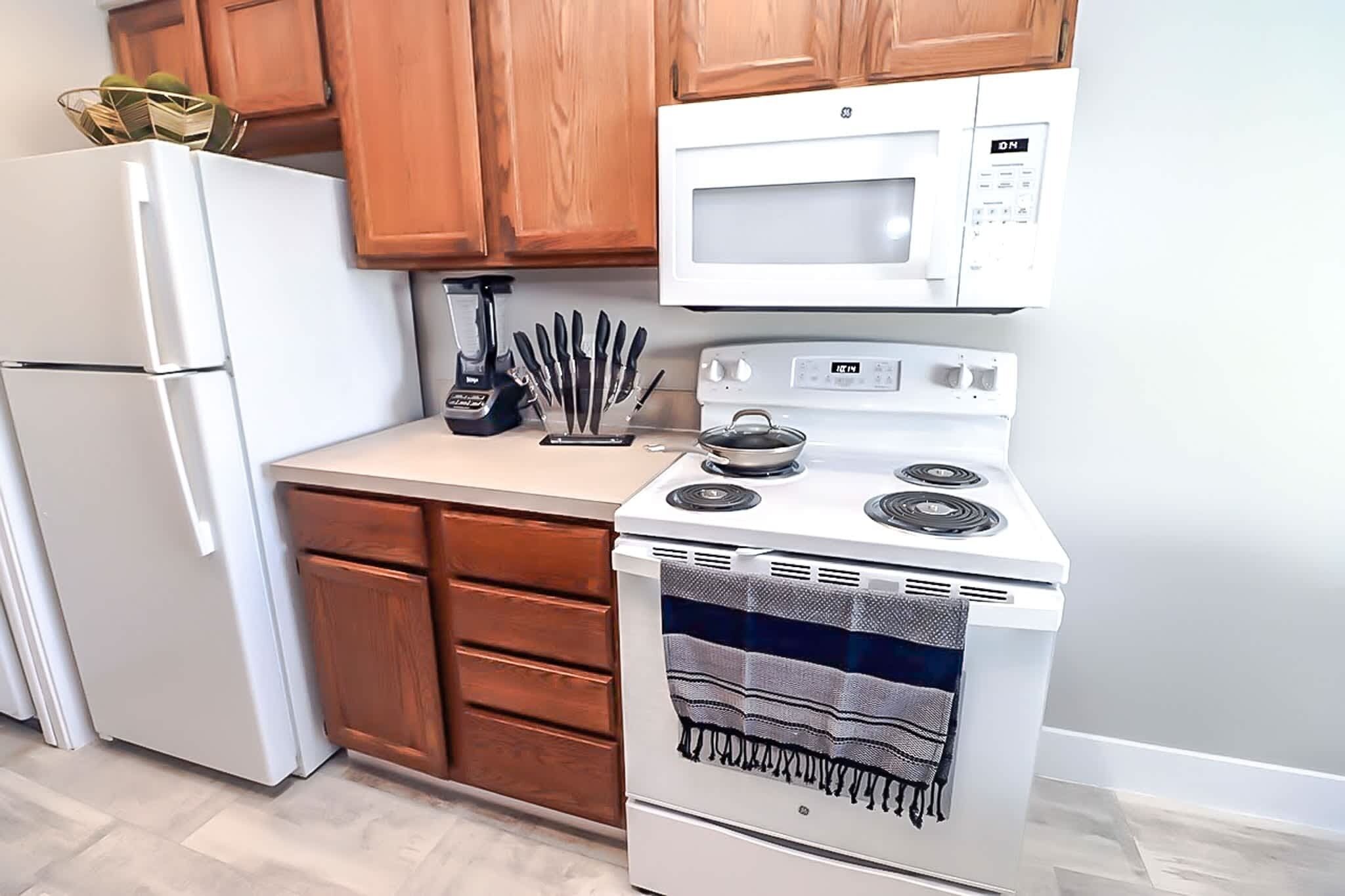 Una cocina con nevera blanca, microondas, cocina y armarios de madera.