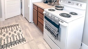 Une cuisine de taille réduite avec des meubles en bois, un réfrigérateur blanc, un four à micro-ondes, une cuisinière et un tapis à motifs.
