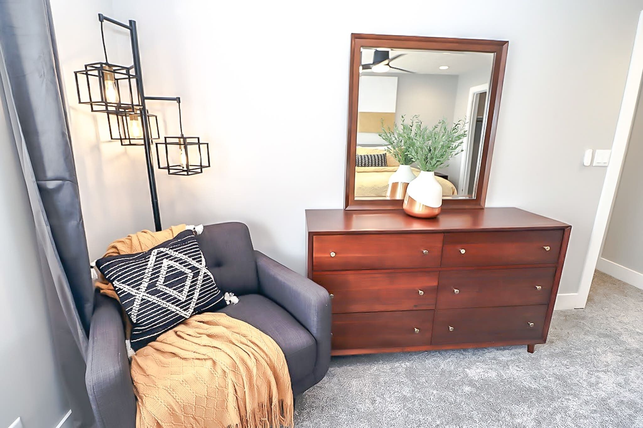 A modern living room with a dark leather sofa, a wooden dresser, a large mirror, and a geometric wall light fixture.