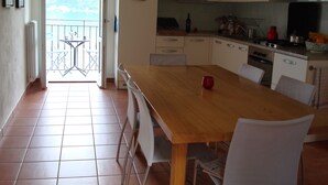 A kitchen with a wooden table, white chairs, a red cup, and a view of the sea through an open door. - Dream view - Spacious apartment with large garden (Lezzeno)