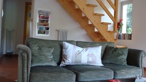 A living room with a green sofa, a wooden staircase, a radiator, and a window with a view of greenery. - Dream view - Spacious apartment with large garden (Lezzeno)